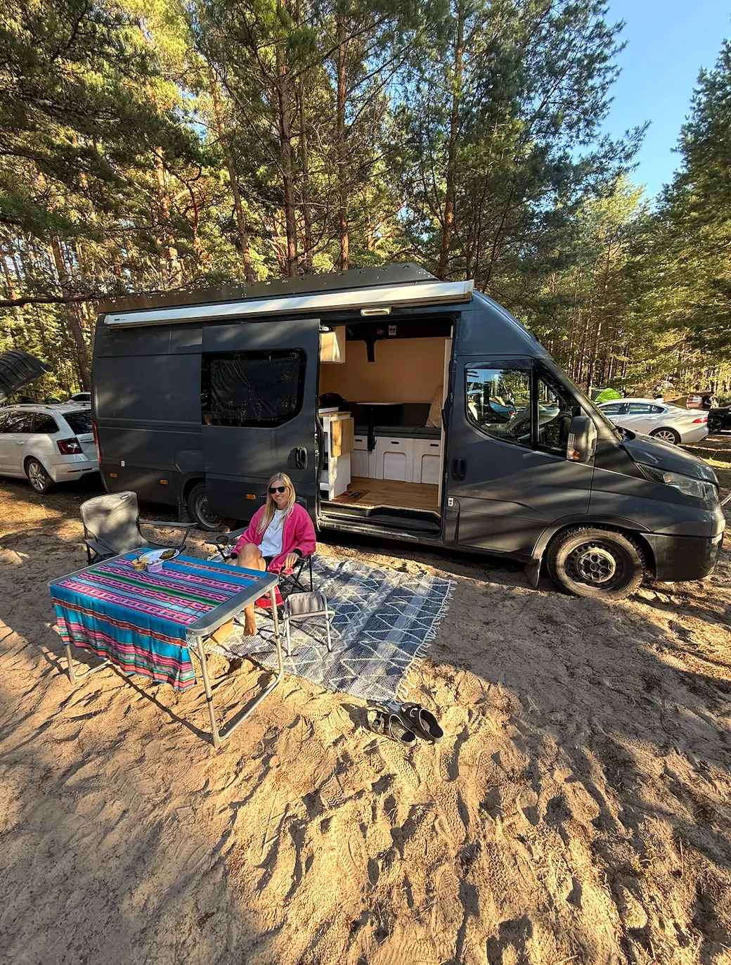 Liina relaxing beside WakeVan at a woodland campsite